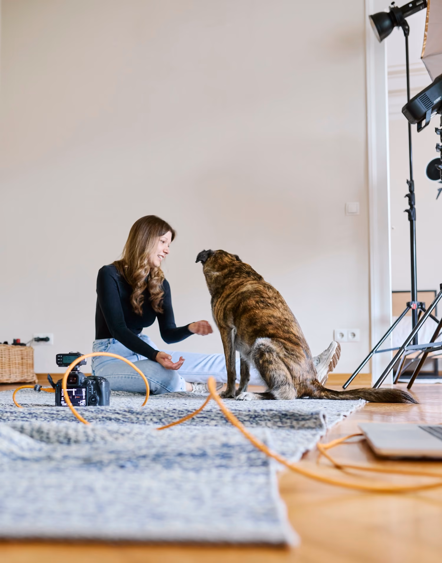 Woman sitting on floor smiling at a seated dog in a photo studio with camera and lights nearby.