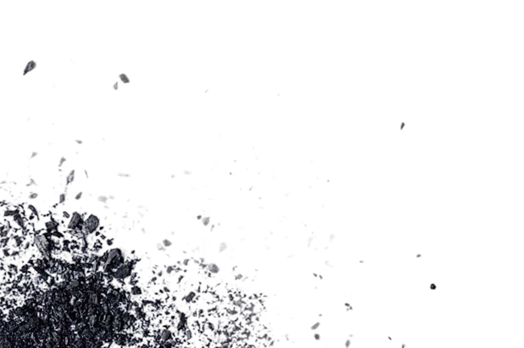 Close-up of charcoal pieces with small fragments breaking off against a black background.