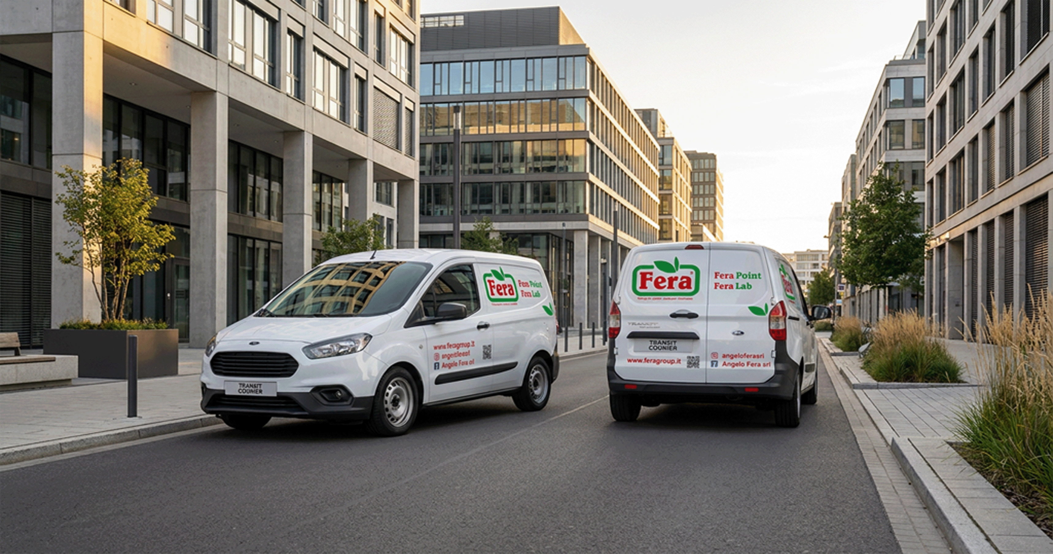 Two white Ford Transit Connect vans with Fera logos parked on a city street between modern buildings.