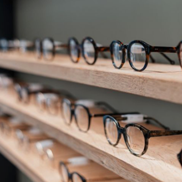 Multiple pairs of eyeglasses displayed on wooden shelves in an eyewear store.