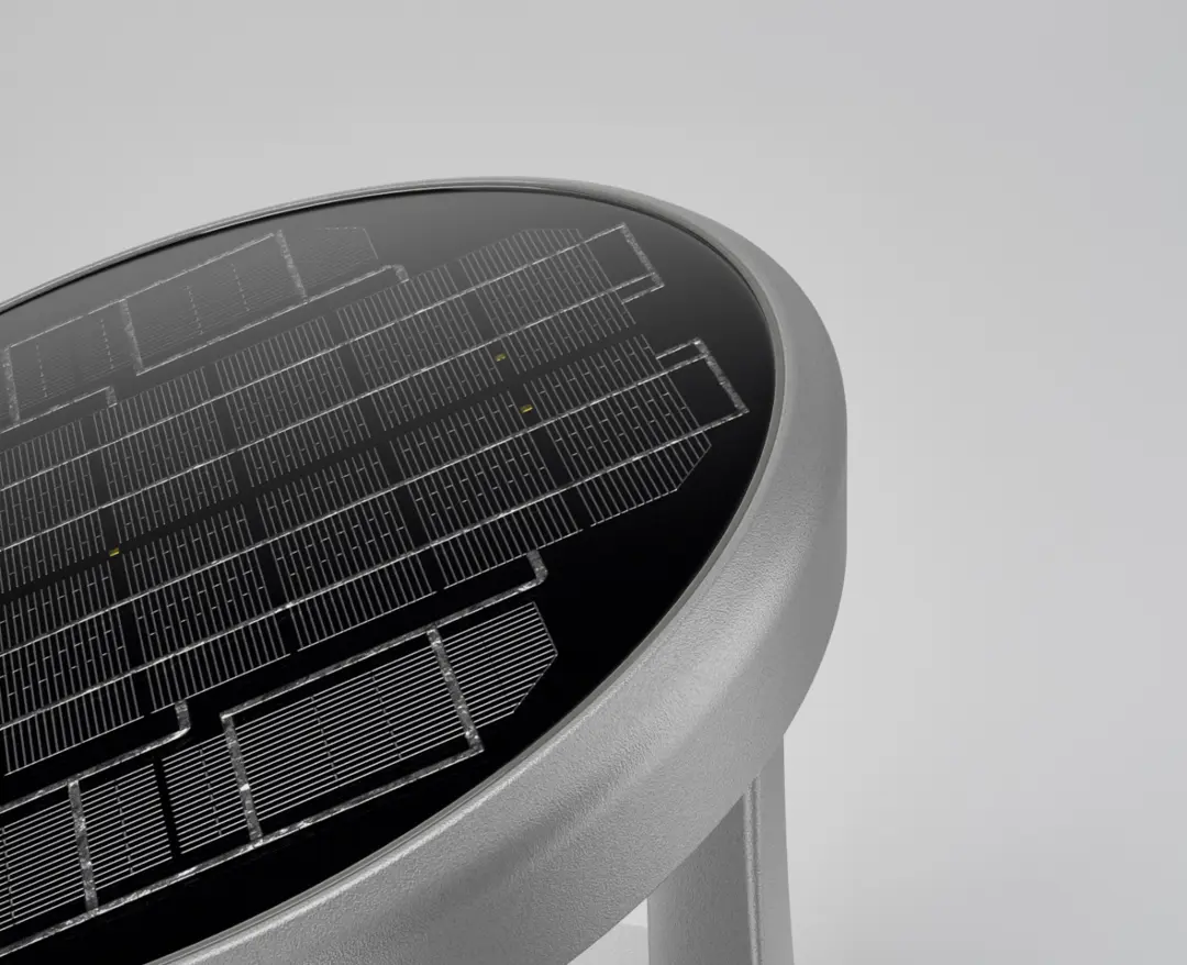 Close-up of a round solar panel embedded in a metallic grey frame on a light grey background.