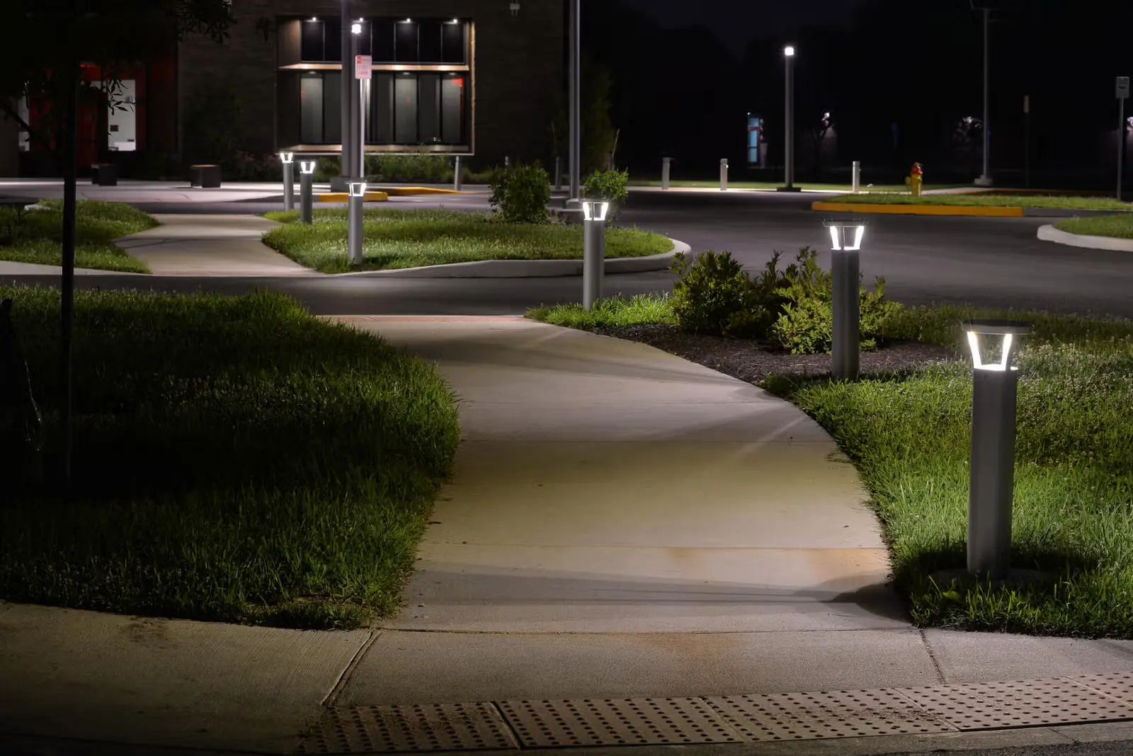Well-lit sidewalk winding through grassy areas with modern lamp posts at night.