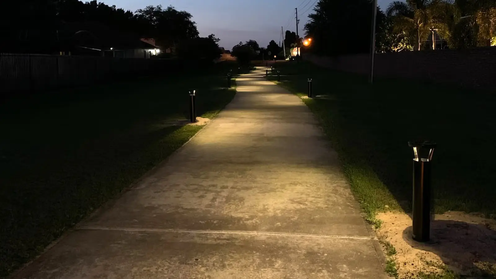 A dimly lit concrete pathway at night with small black bollard lights lining both sides.