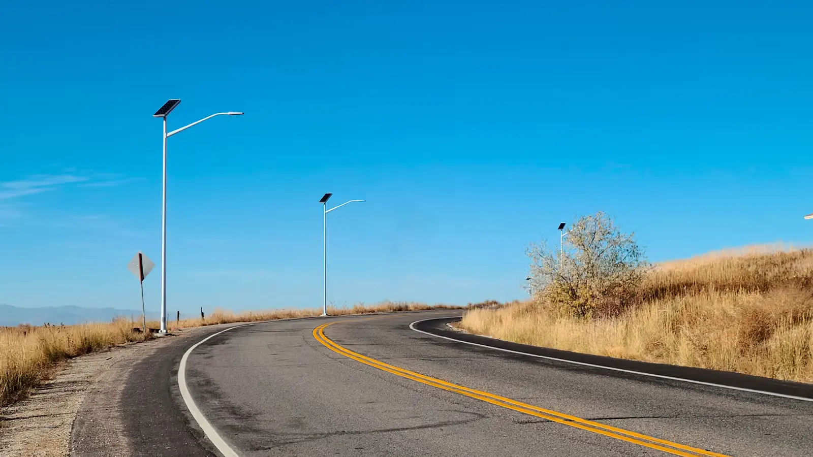 Curved rural road with solar-powered streetlights under a clear blue sky.