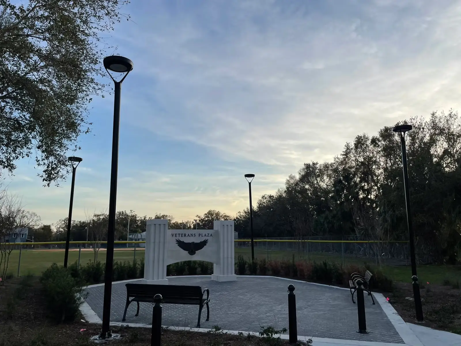Veterans Plaza with benches, lamp posts, and a white monument featuring an eagle silhouette under a partly cloudy sky.