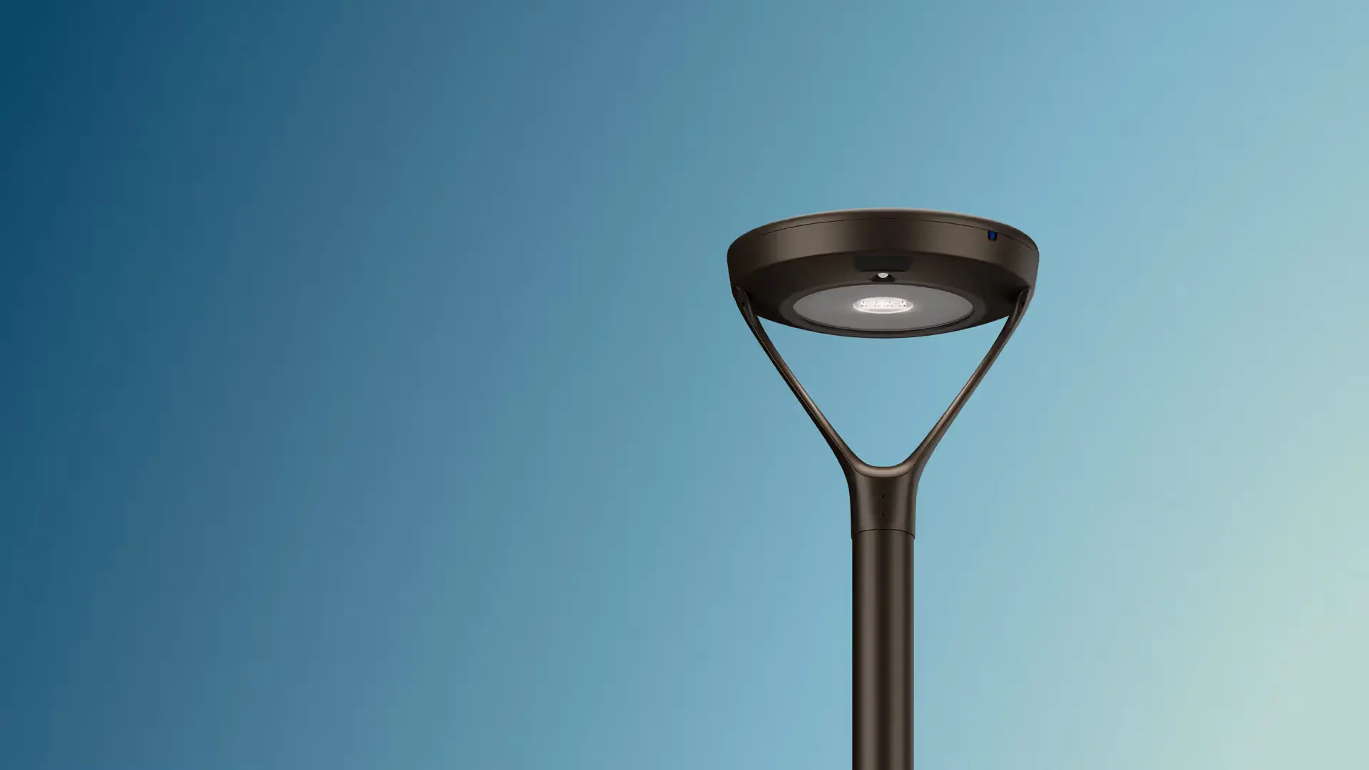 Modern black street lamp with circular LED light fixture against a gradient blue sky.