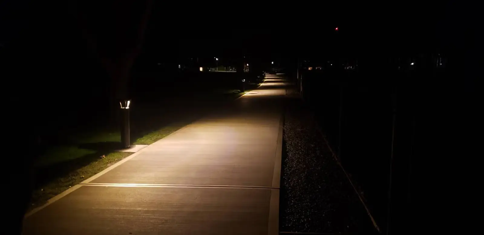 Dimly lit concrete sidewalk at night with small ground lights on the left side.