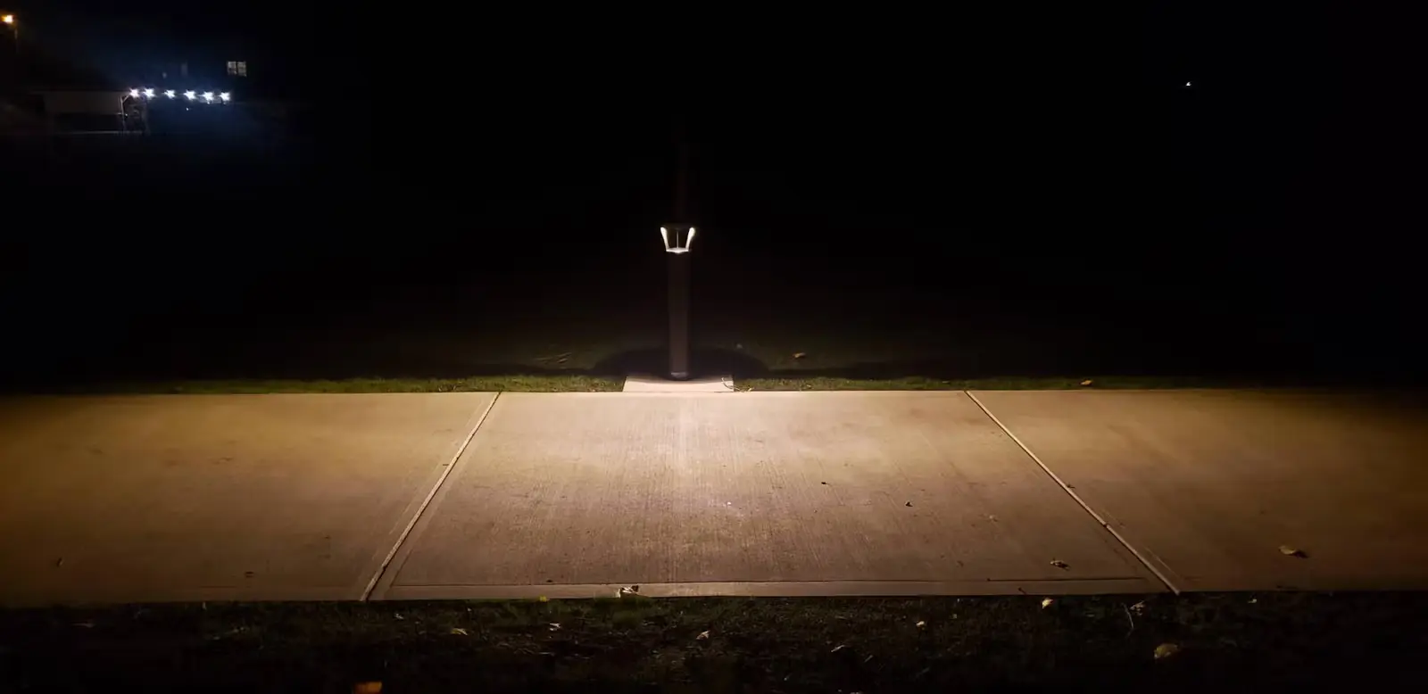 A single modern bollard light illuminating a concrete pathway at night.