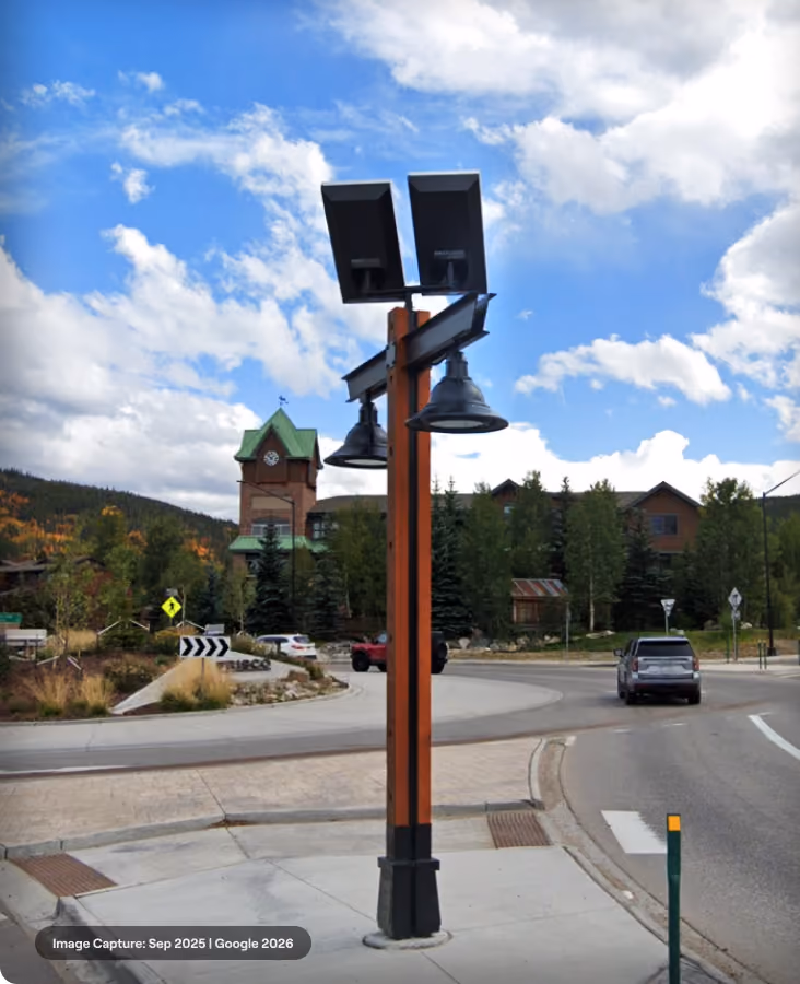 Wooden pole with solar panel and light fixture against blue sky near Nordic Center building.