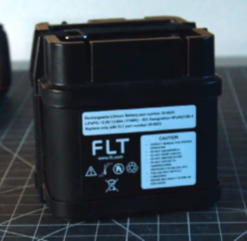 Black rechargeable lithium-ion battery with a white caution label on a grid surface.