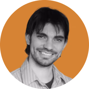 Smiling man with dark hair and beard wearing a light striped shirt on an orange background.