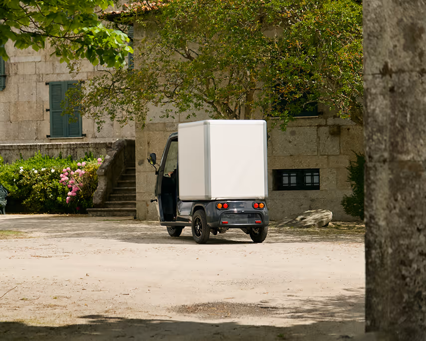SmarTuk L2 steht in einem begrünten Innenhof vor einem alten Steingebäude.