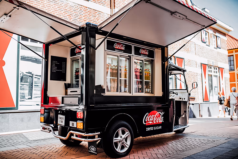 L5 Cargo als mobiler Coca-Cola-Zero-Sugar-Verkaufswagen mit geöffnetem Dach und Getränkekühlschränken in einer gepflasterten Innenstadtstraße.