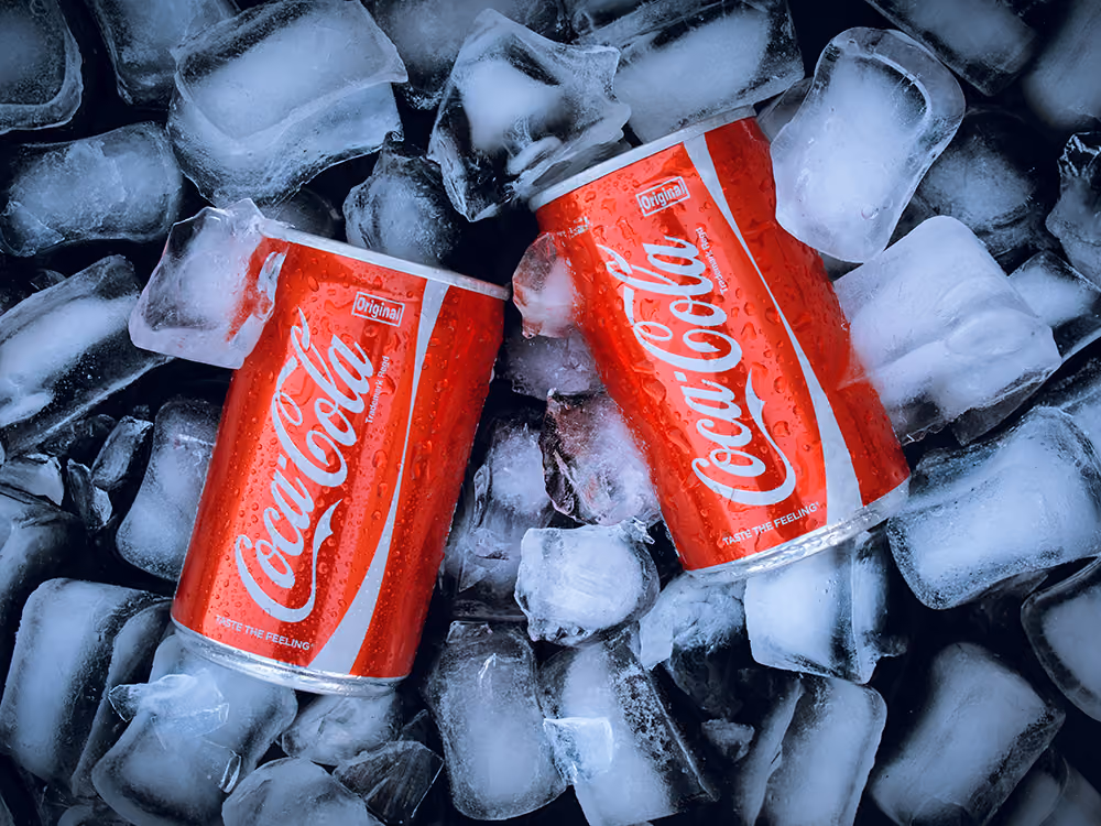 Zwei rote Coca-Cola-Dosen liegen zwischen zahlreichen Eiswürfeln.