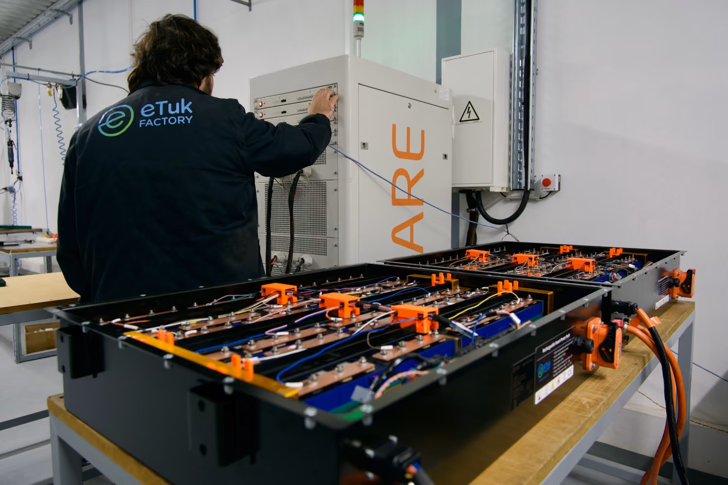 Ein Techniker in einer eTuk-Factory-Werkstatt prüft elektrische Batteriesysteme und offene Akkumodule auf einer Werkbank.