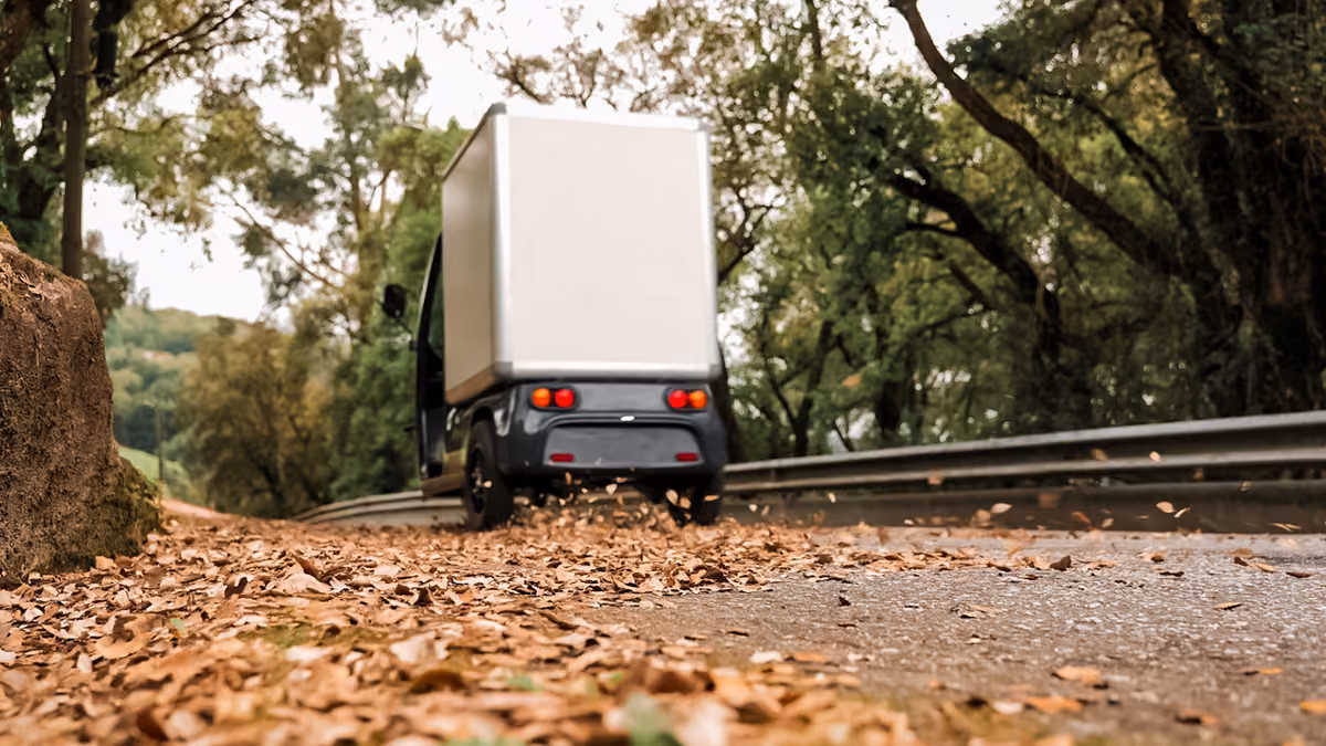 Ein SmarTuk L2 fährt auf einer von Herbstlaub bedeckten Straße durch ein bewaldetes Gebiet.