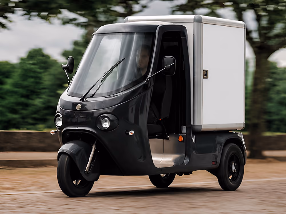 Elektrisches Lieferfahrzeug SmarTuk L2 fährt auf einer gepflasterten Straße durch eine baumbestandene Landschaft.