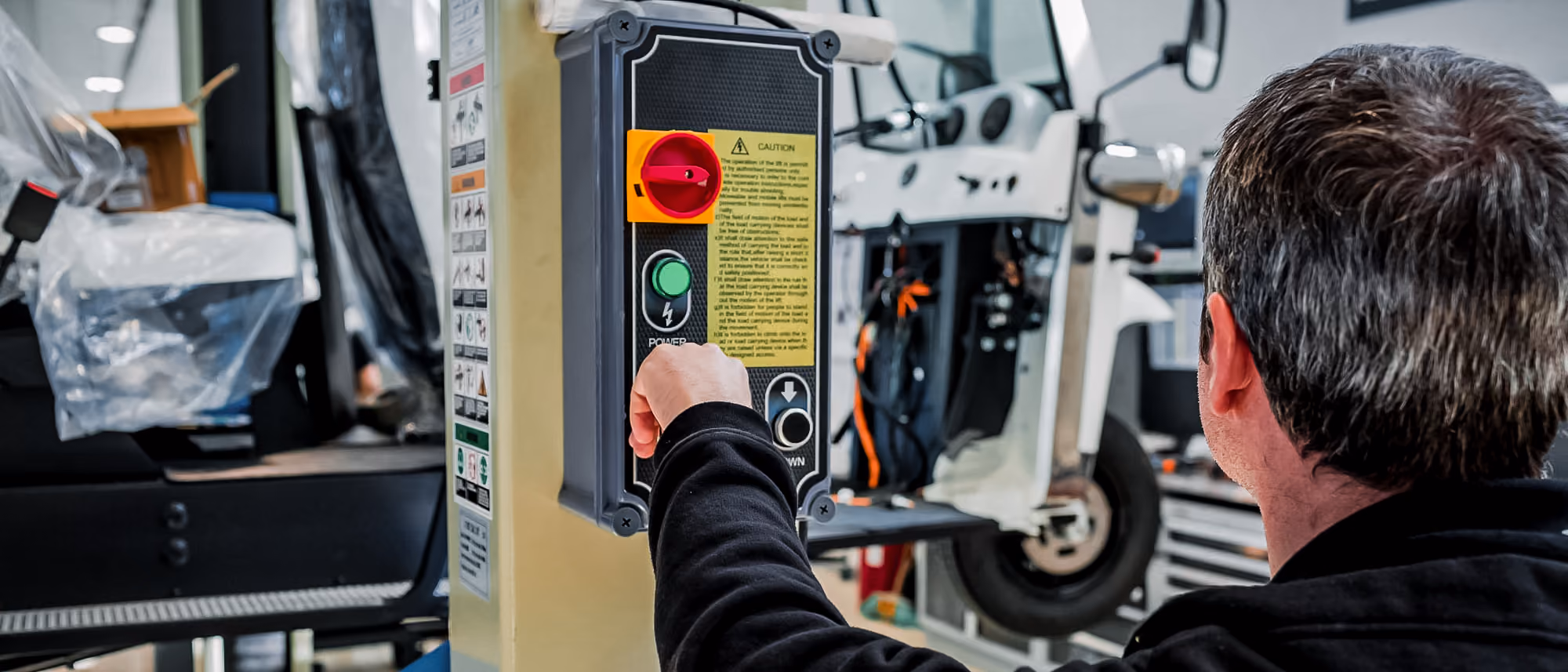 Mitarbeiter bedient das Steuerpanel einer Hebebühne in einer Werkstatt, während im Hintergrund ein L5 Limo GT angehoben ist.