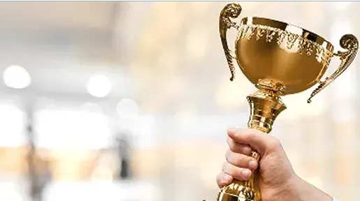 Hand holding a golden trophy cup against a blurred background.