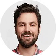 Smiling bearded man with dark hair wearing a red and gray plaid shirt.