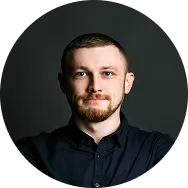Portrait of a man with short hair and a beard wearing a black shirt against a dark background.