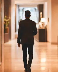A man in a dark jacket walking down a softly lit hotel corridor
