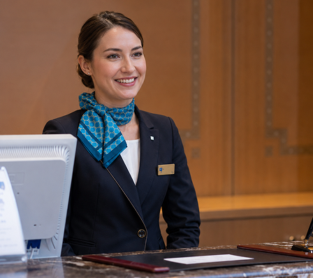 A smiling concierge in uniform standing at a reception desk