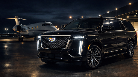 A black Cadillac Escalade parked beside a private jet at night