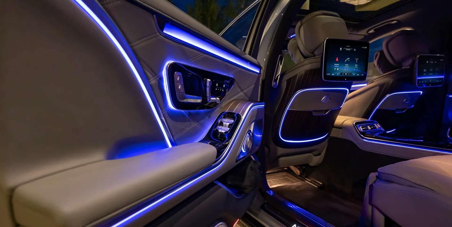 The illuminated interior of a luxury car with blue ambient lighting and a rear-seat entertainment screen