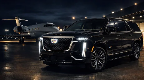 A black Cadillac Escalade parked beside a private jet at night