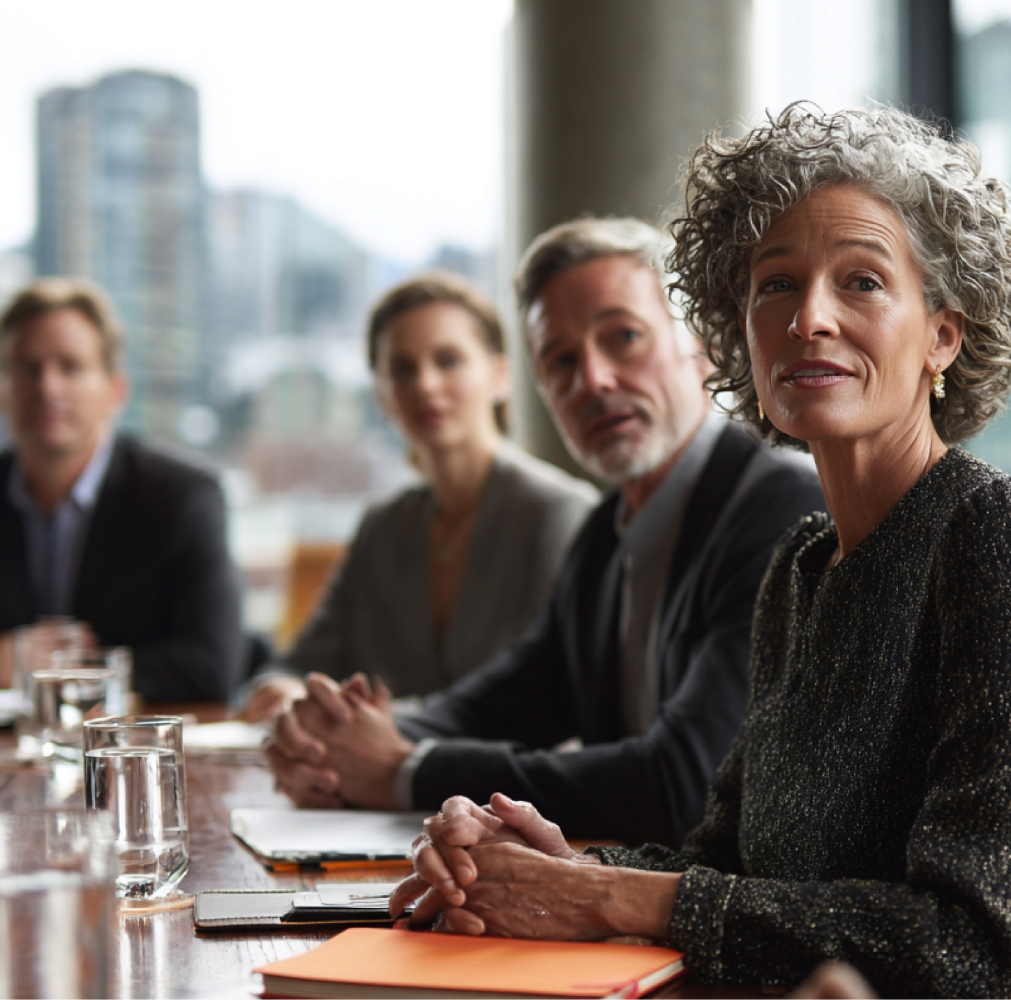 Four businesspeople sitting at a conference table listening during a meeting in an office.