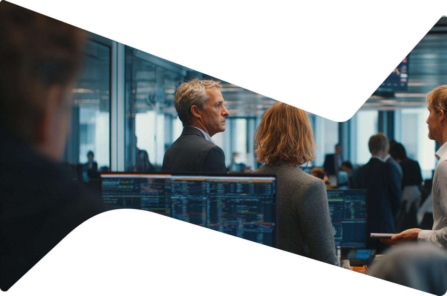 Professionals in a modern office with computer screens displaying data and stock market info.