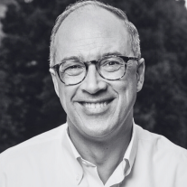 Smiling man wearing glasses and a white shirt with a dark blurred background.