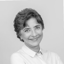 Smiling person with short curly hair wearing a light-colored shirt against a plain background.