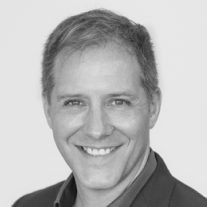 Smiling man with short hair wearing a dark blazer in a black and white photo.