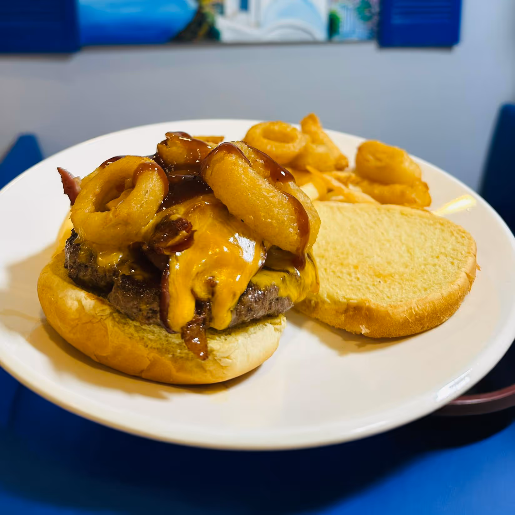 Cheeseburger with bacon and onion rings on a toasted bun, served with curly fries on a white plate.