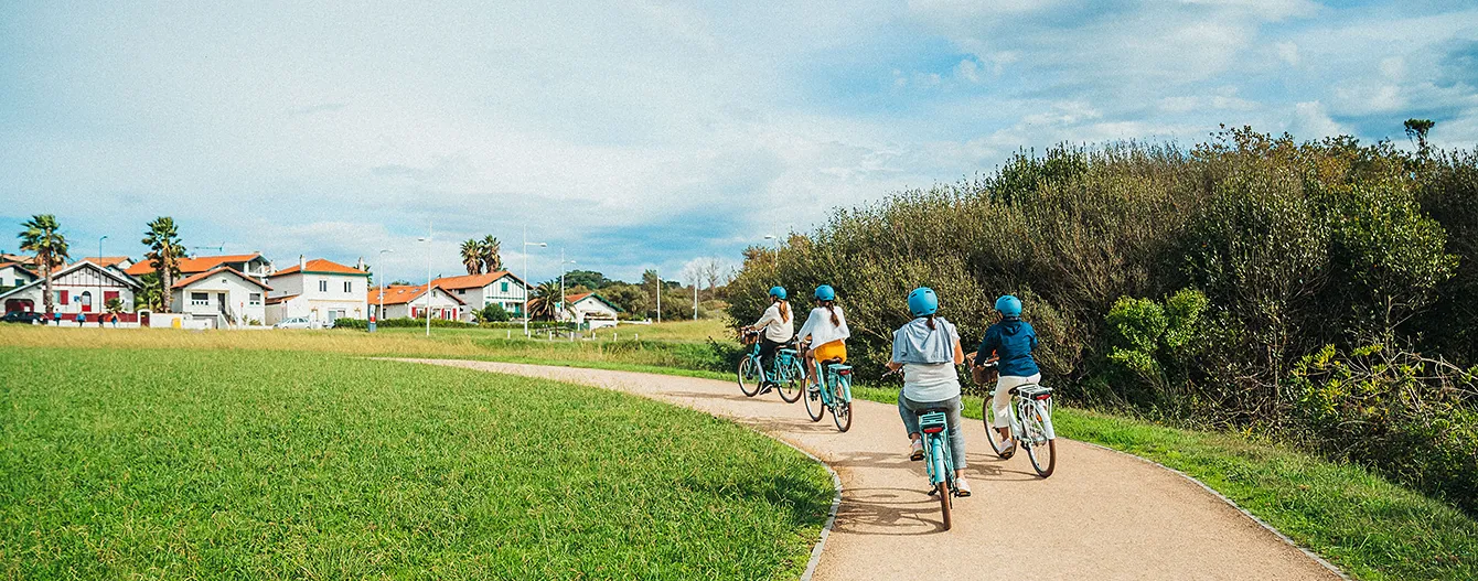Quatre personnes portant des casques bleus font du vélo électrique sur un chemin courbe près de maisons.
