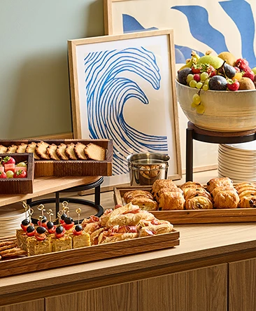 Buffet avec plateaux de viennoiseries, sandwichs, toasts garnis et bol de fruits frais colorés.