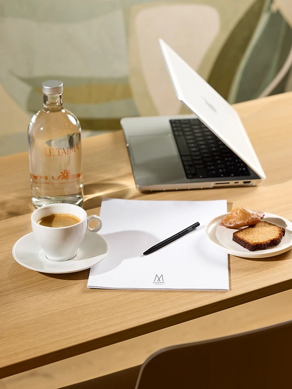 Bureau avec un ordinateur portable, bouteille d'eau, tasse de café, stylo, feuilles et assiette de pâtisseries.