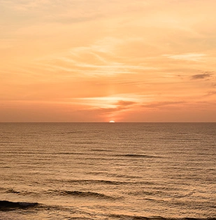Soleil couchant au-dessus de la mer calme sous un ciel orange doux.