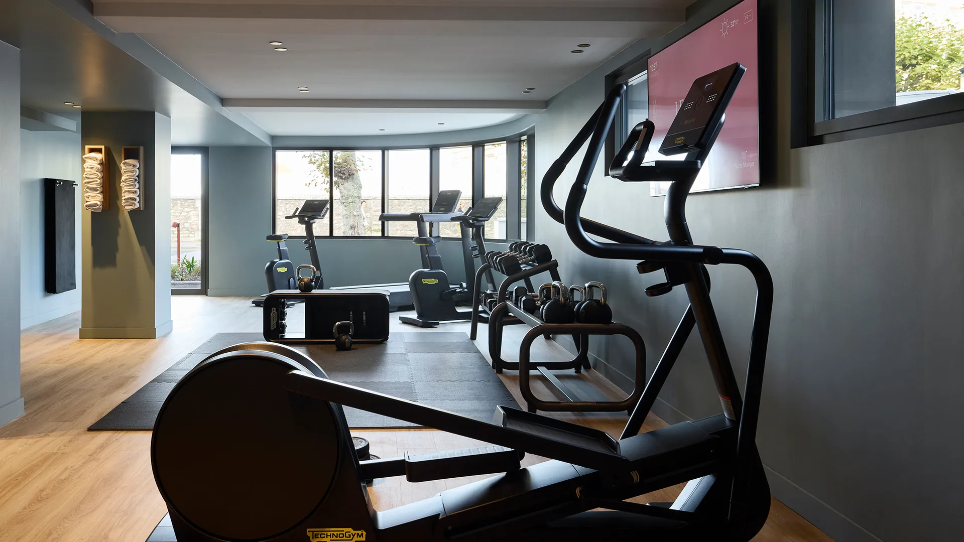 Salle de sport moderne avec vélo elliptique, tapis de course, kettlebells et poids libres.