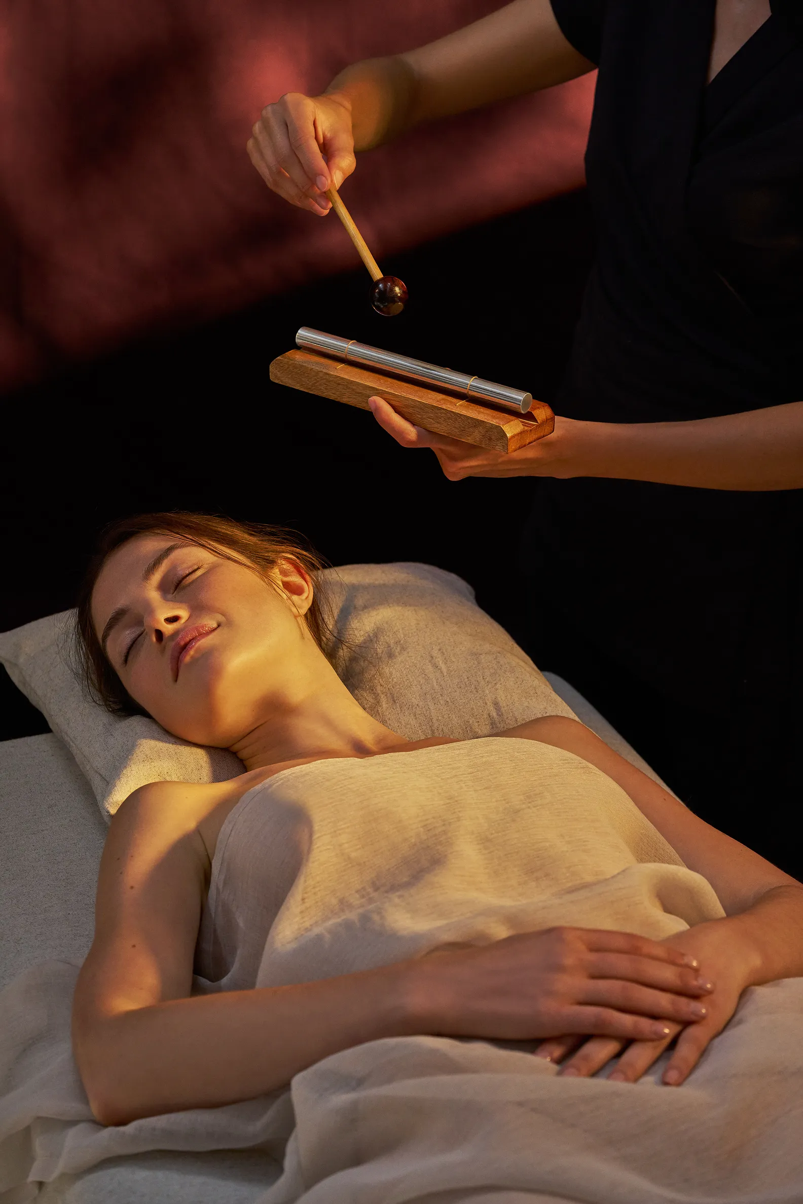 Femme allongée, yeux fermés, recevant un soin sonore avec un bâton de musique.