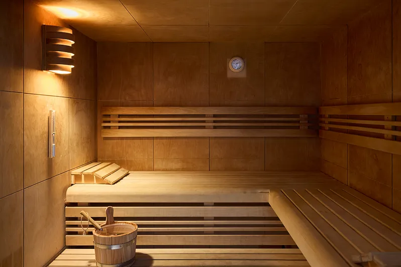 Intérieur d'un sauna en bois avec bancs, seau et louche, éclairage tamisé chaleureux.