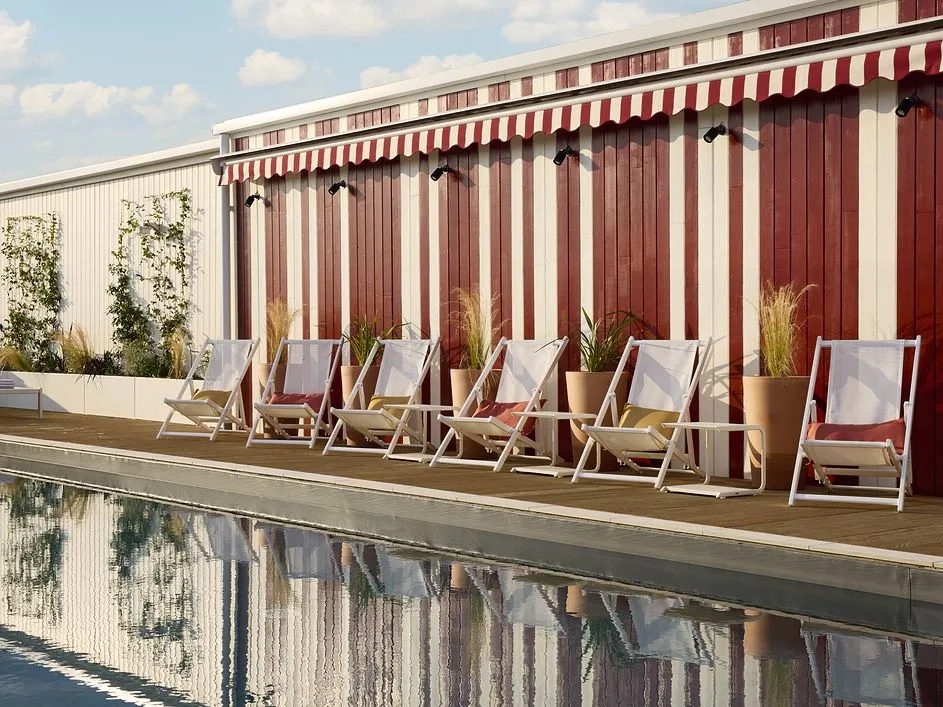 Poolside with white lounge chairs and cushions in front of a red and white striped wall.