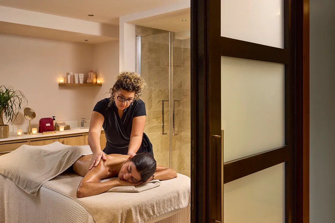 A woman receives a relaxing massage in a warm spa room with burning candles.