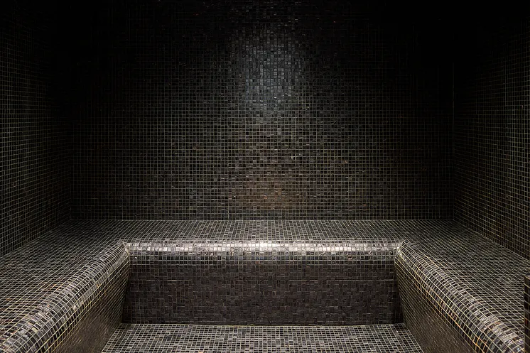Black mosaic bench and walls in a dark and uncluttered room.