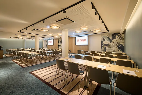 Modern conference room with rows of tables and chairs, screen displaying Le Talaia.