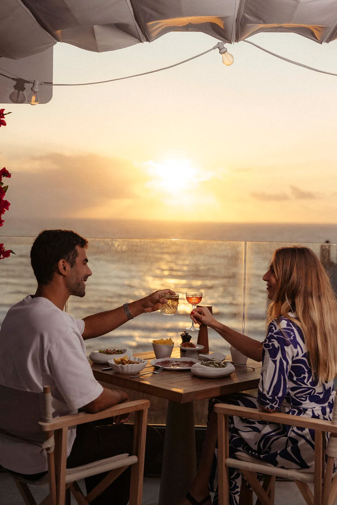 Couple toasting with drinks at sunset at a table near the sea.