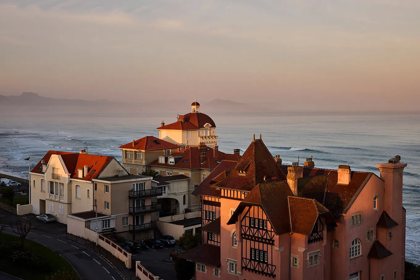 Maisons avec toits rouges près de la mer au coucher du soleil avec montagnes à l'horizon.
