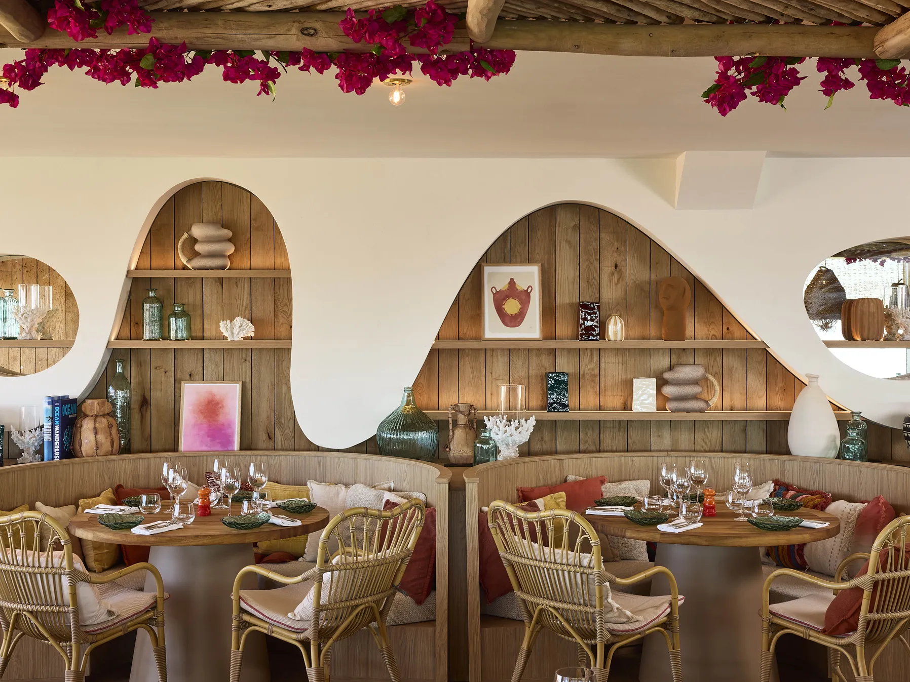 Coin repas élégant avec fauteuils en rotin, coussins colorés, décorations murales et étagères en bois.